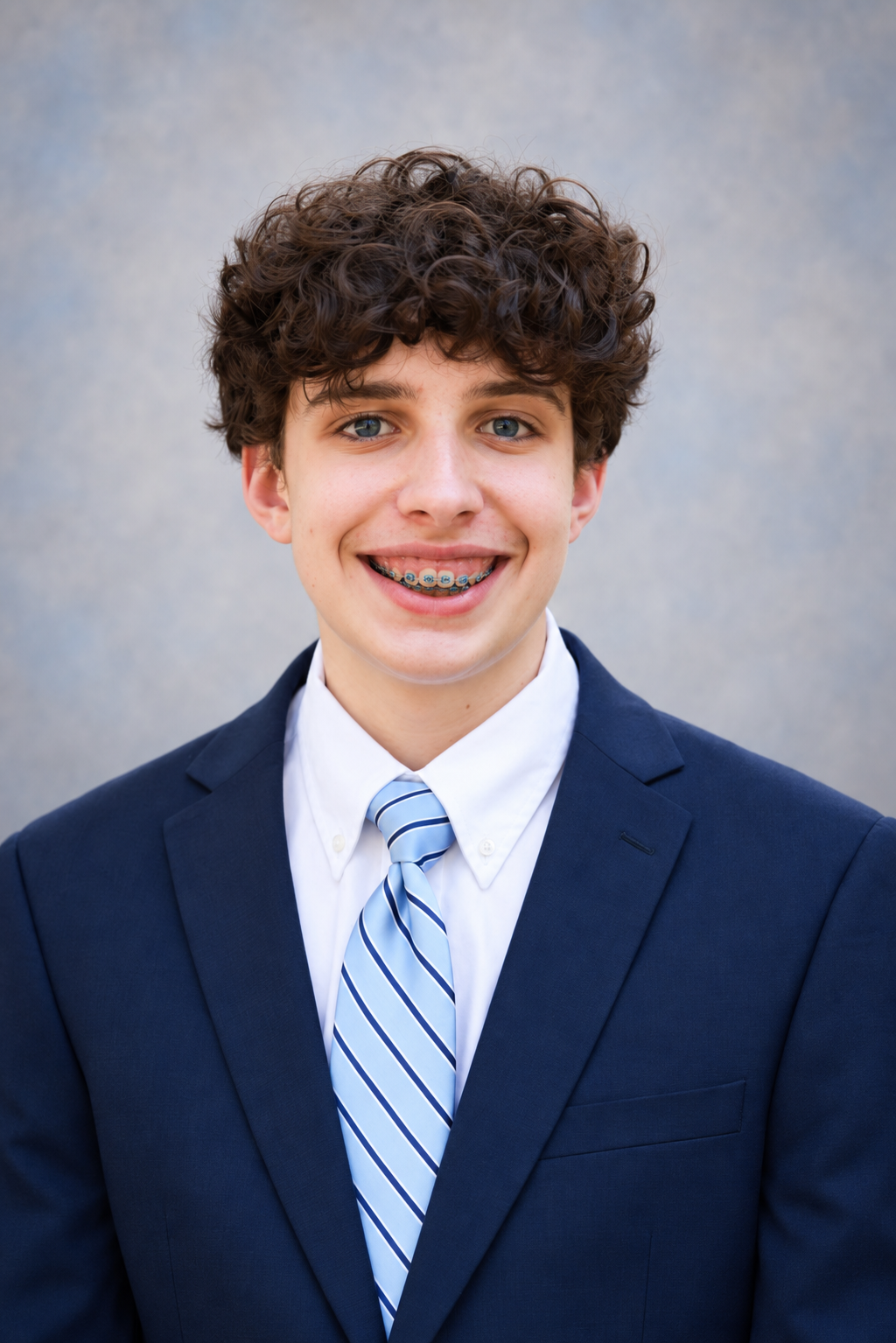 Headshot of Noah Harrelson smiling in a navy suit and blue striped tie against a gray background